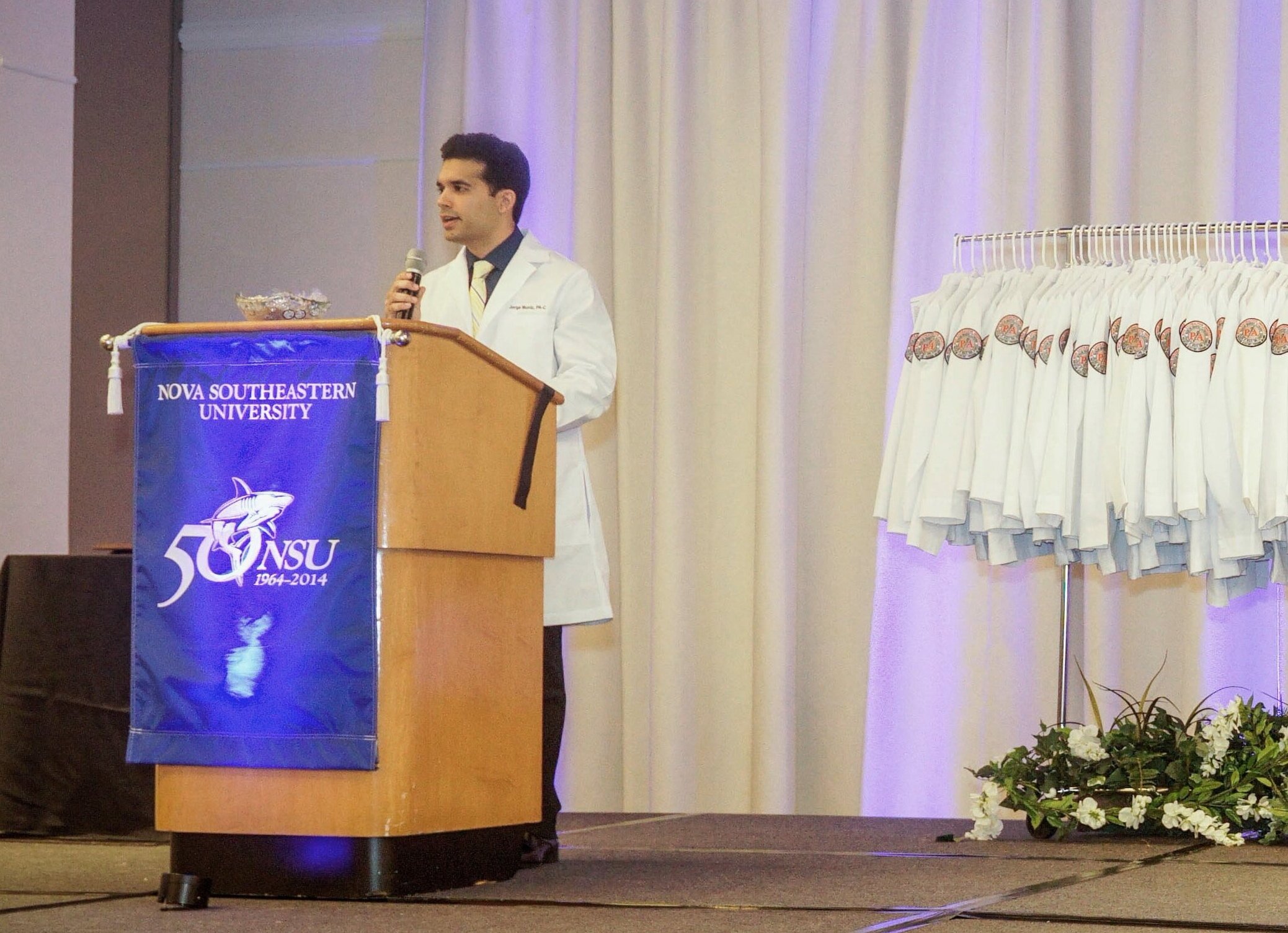 Jorge Muniz speaking at a podium in a white coat